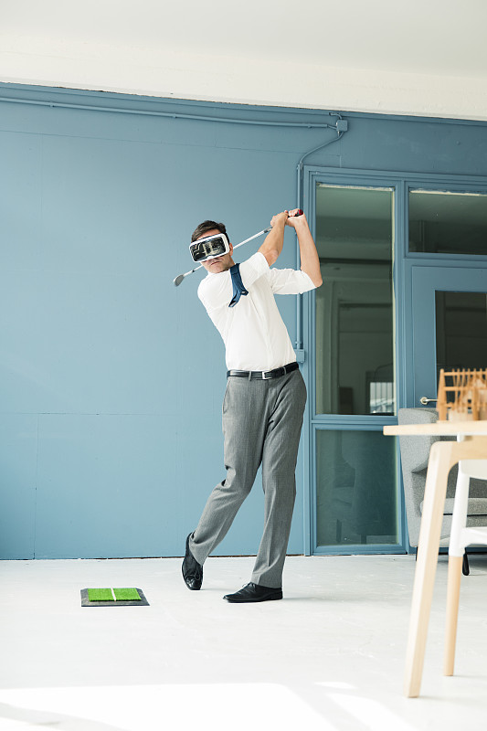 商人戴著VR眼鏡在辦公室打高爾夫圖片素材