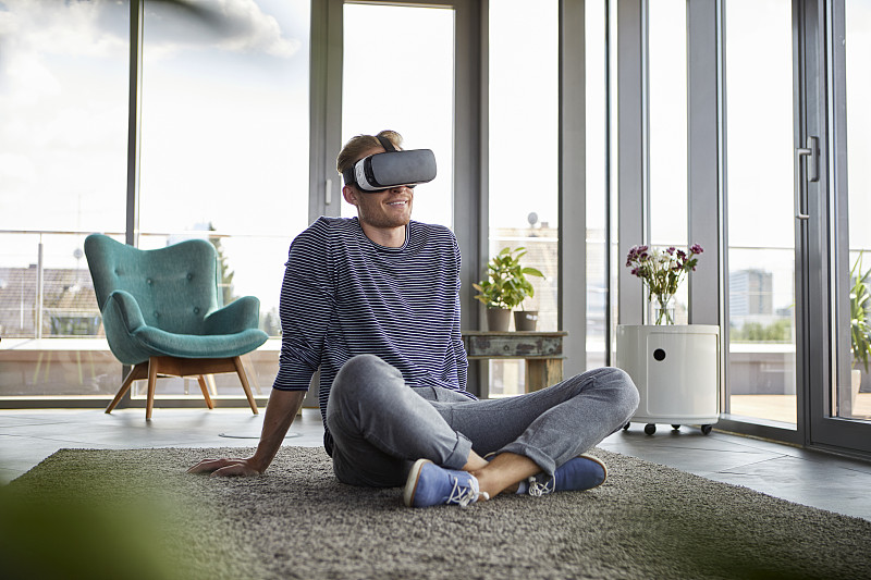 年輕人坐在家里的地毯上，戴著VR眼鏡圖片素材