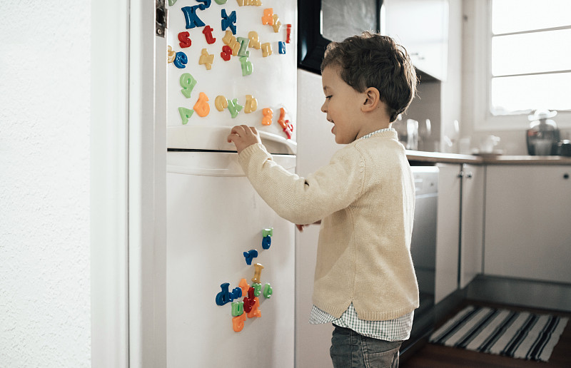 小男孩在玩冰箱上的磁鐵文字圖片素材