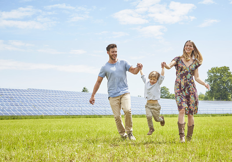 父親和母親牽著兒子的手，走過太陽能農場旁的田野圖片下載