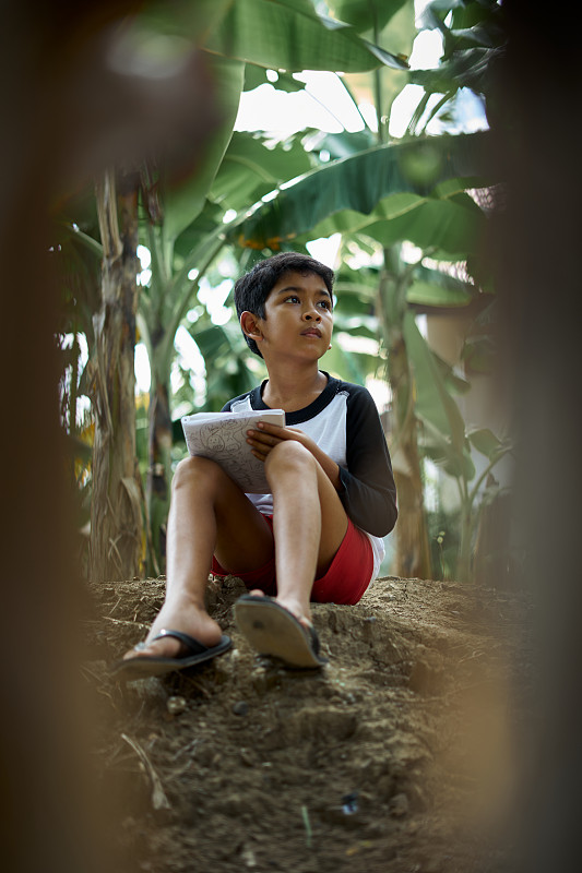在印度尼西亞巴厘島的森林里，一個男孩拿著筆記本學習圖片素材