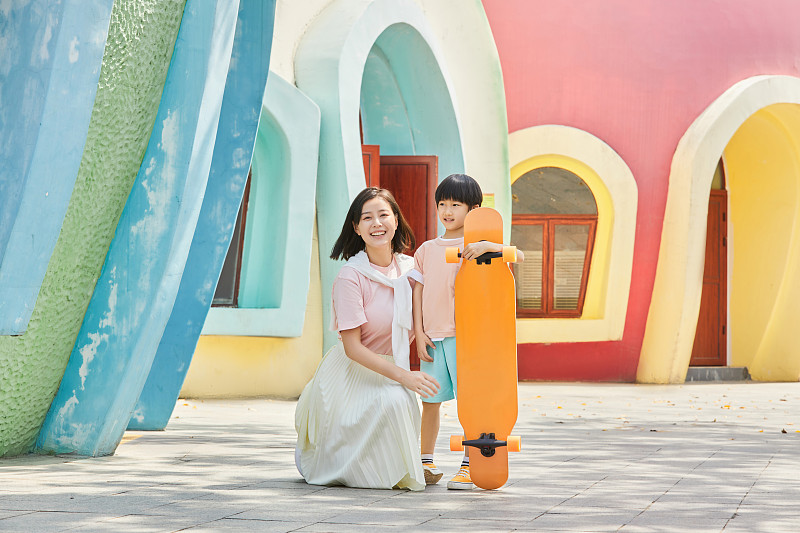 陪伴孩子一起玩滑板的年轻妈妈图片下载