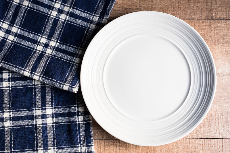 在舊的木制棕色背景上，空的餐巾白色盤子，俯視圖。圖像與復制空間。廚房桌子與毛巾和一個盤頂視圖與復印空間。圖片素材