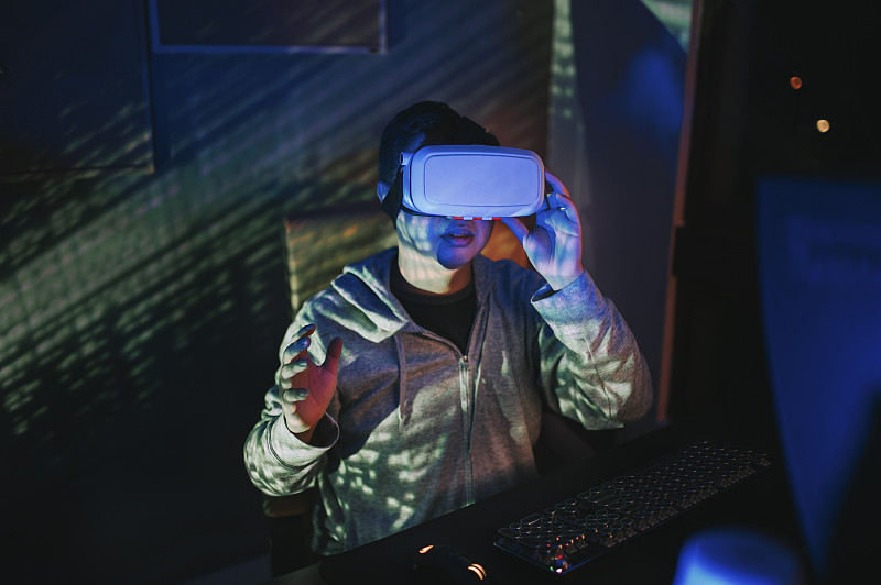 一名亞洲華人男性戴上VR眼鏡，在他的家庭辦公室自修室里，在他的臺式電腦前體驗3D虛擬游戲體驗圖片素材