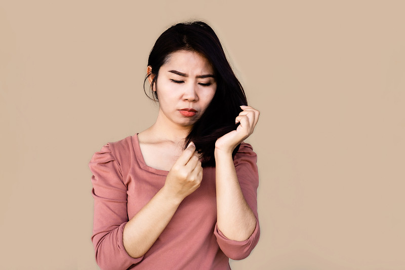 不快樂的亞洲女人手握著她受損的分叉頭發圖片素材