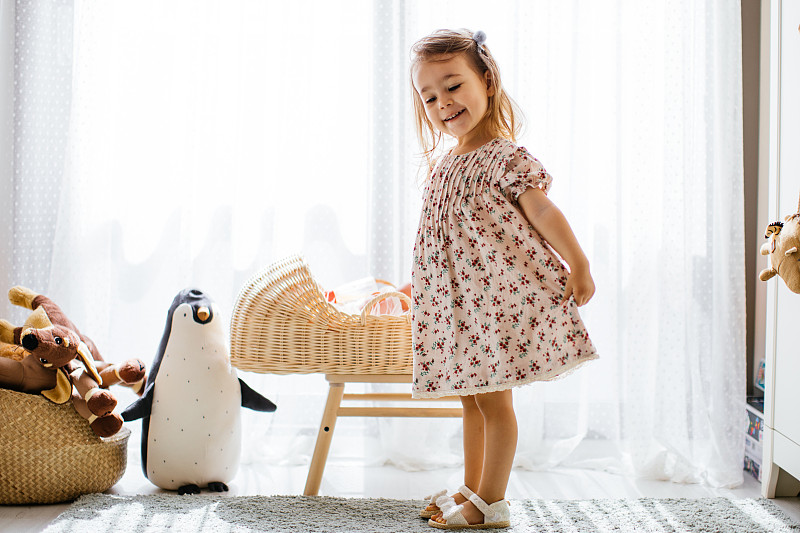 可愛的小女孩在嬰兒床里喂她的玩具娃娃，在有大窗戶的陽光臥室里玩圖片素材