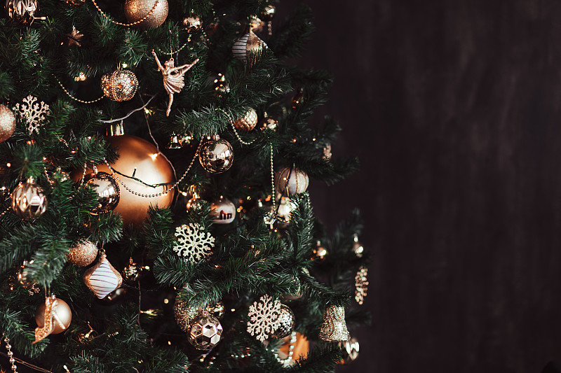 金色的圣誕裝飾品在發光的圣誕樹在黑色的背景。圖片素材