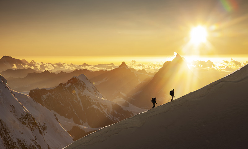 日出時，攀登者在白雪皚皚的山脊上圖片素材