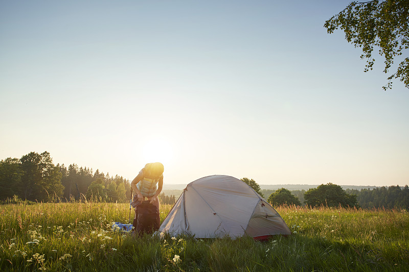 日落時分，孤獨的女性在茂盛的草地上搭起帳篷攝影圖片
