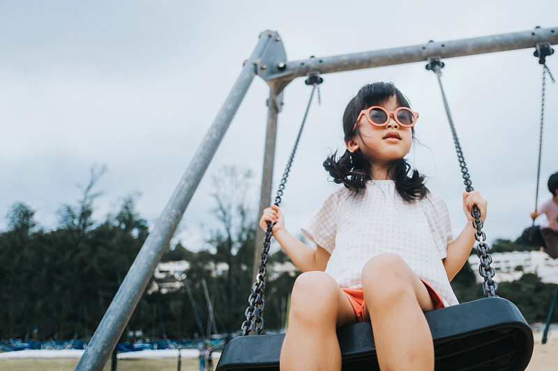 可愛的亞洲小女孩戴著太陽鏡在戶外操場上玩秋千。在戶外享受夏日。童年的生活方式，無憂無慮和自由的觀念圖片下載