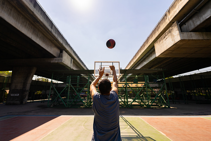亞洲運動員在陽光明媚的戶外場地練習投籃。圖片下載