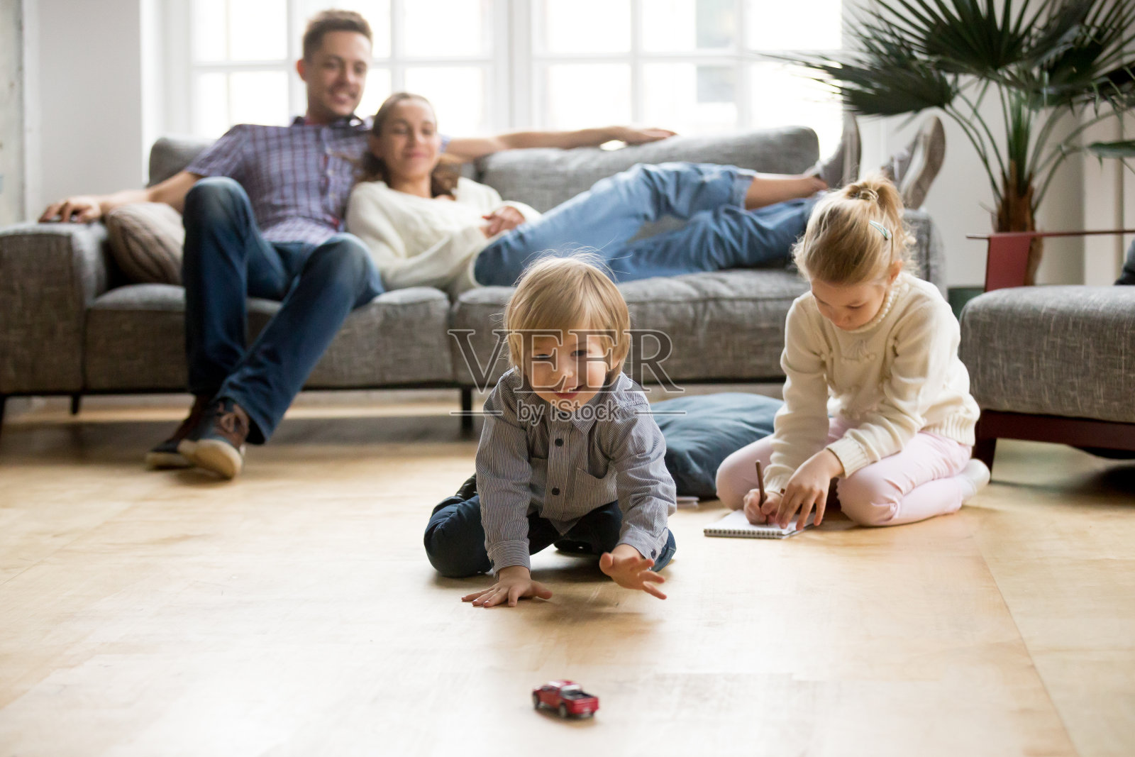 孩子們在地板上玩耍，父母們在家里的沙發上放松照片攝影圖片