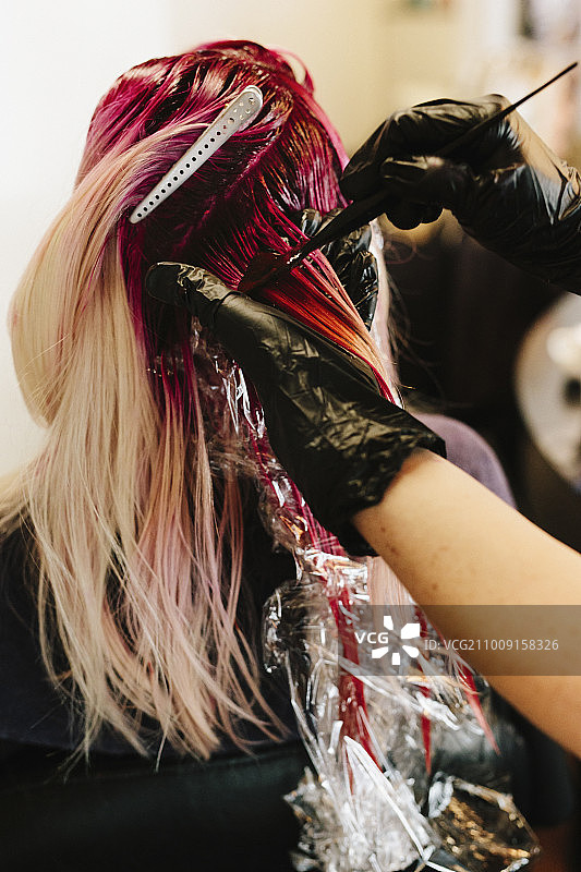 染发师将粉红色的头发涂在客户的金色长发上。图片素材