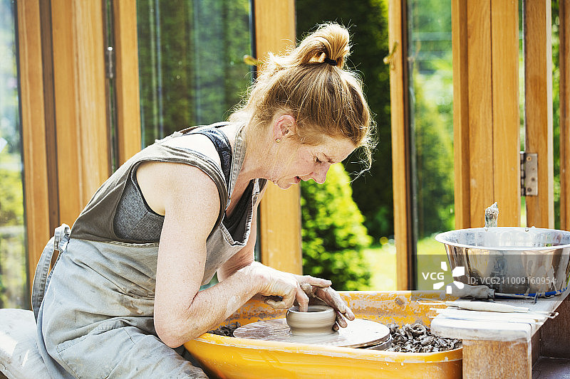 在她的作坊里，一个妇女在陶工转盘上制作陶土。图片素材