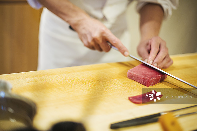 在小型商业厨房工作的厨师，用一把大刀切鱼来做寿司的厨师图片素材