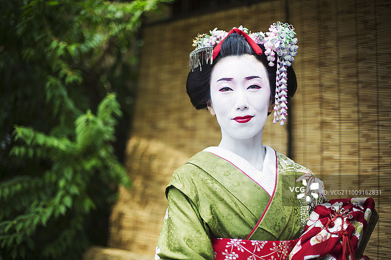 一个穿着传统艺妓风格的女人，穿着和服和宽腰带，精心设计的发型和花发夹，白色的脸化妆，明亮的红色嘴唇和黑色的眼睛。图片素材