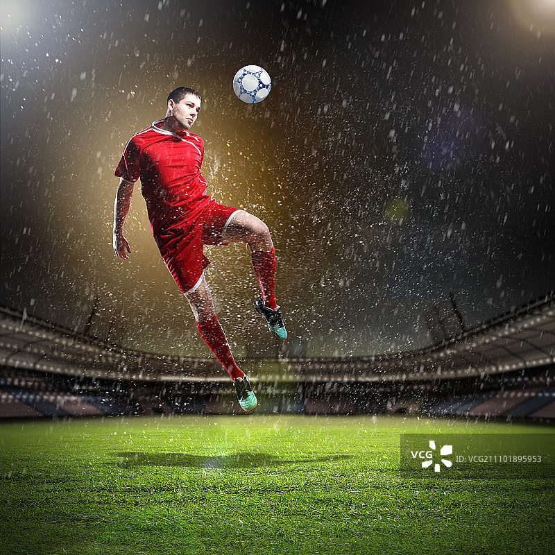 足球运动员击球。穿着红衬衫的足球运动员冒雨在体育场里击球图片素材