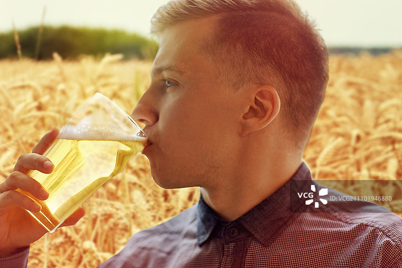 人们，饮料和酒精概念-近距离年轻男子喝啤酒从玻璃谷物田的背景图片素材