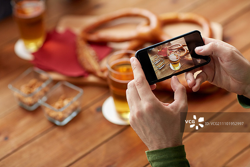 人和技术概念-近距离的手与智能手机图片啤酒和椒盐卷饼在酒吧或酒吧。近距离的手与智能手机图片啤酒图片素材