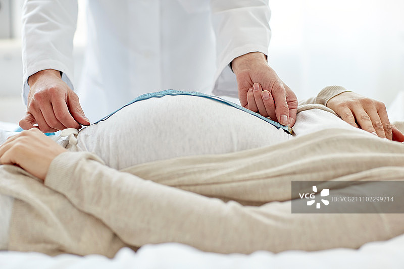 怀孕、医学、保健和人的概念——产科医生在医院用厘米尺测量孕妇的肚子图片素材