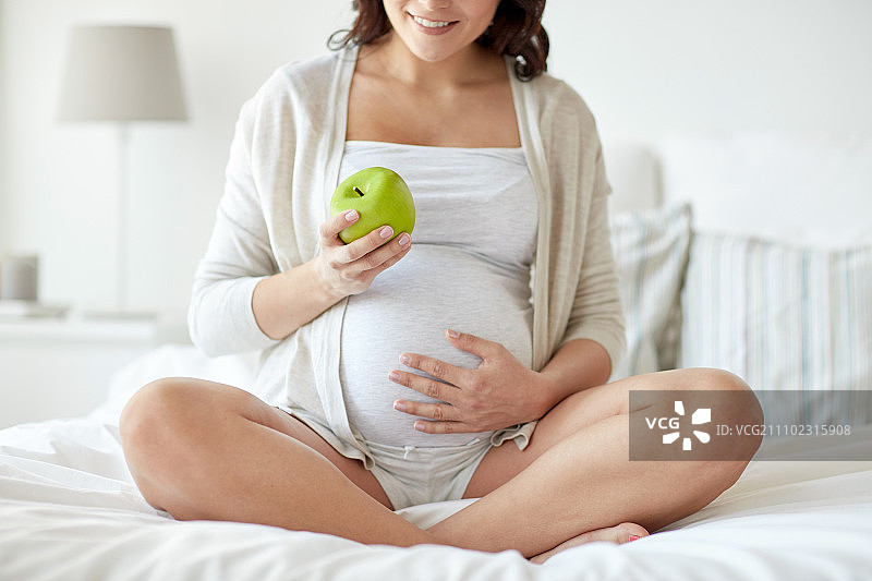 怀孕，健康食品和人们的观念-近距离观察幸福的孕妇在家吃青苹果图片素材