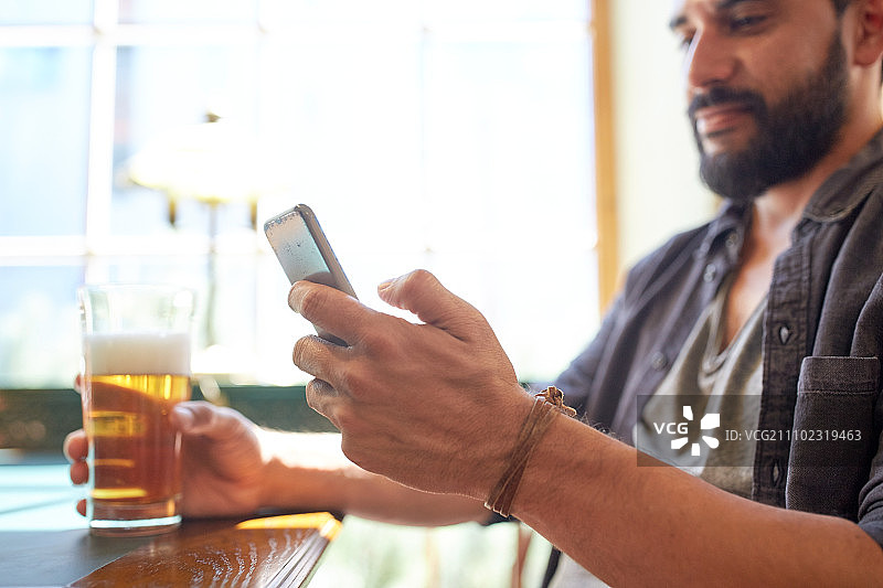 人，休闲和技术概念-近距离的男人与智能手机喝啤酒和阅读信息在酒吧或酒吧图片素材
