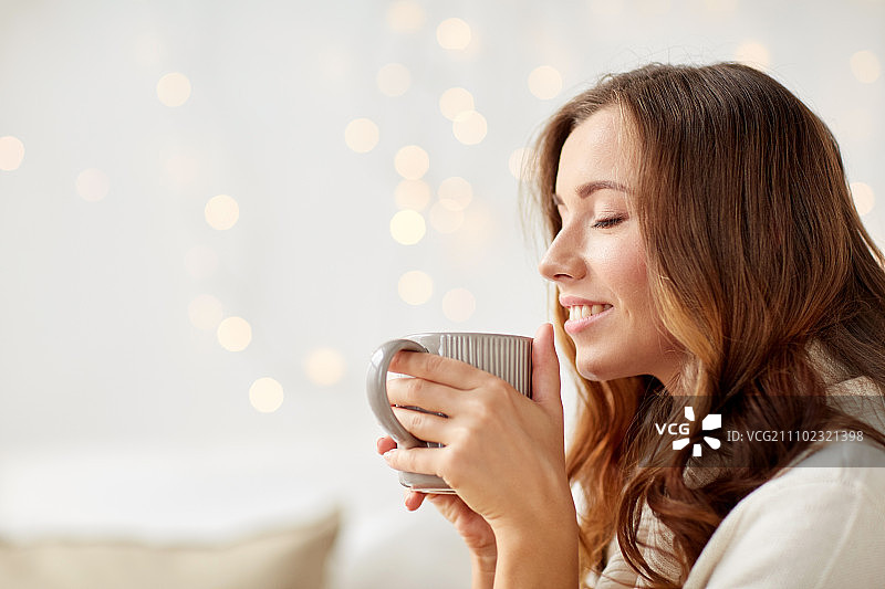 早晨，休闲，圣诞节，冬天和人们的观念——快乐的年轻女子在家里喝一杯咖啡或茶图片素材
