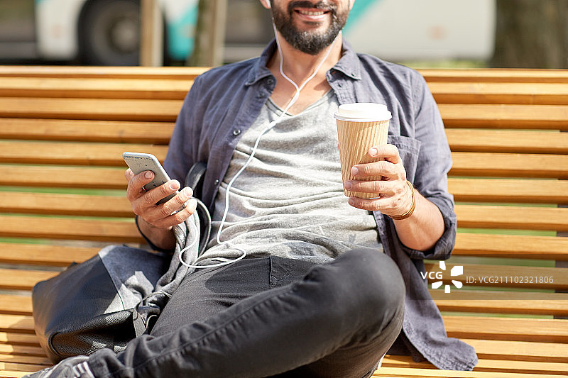 人们，饮料，技术，休闲和生活方式-近距离的男人与耳机和智能手机喝咖啡从一次性纸杯在城市街道长凳图片素材