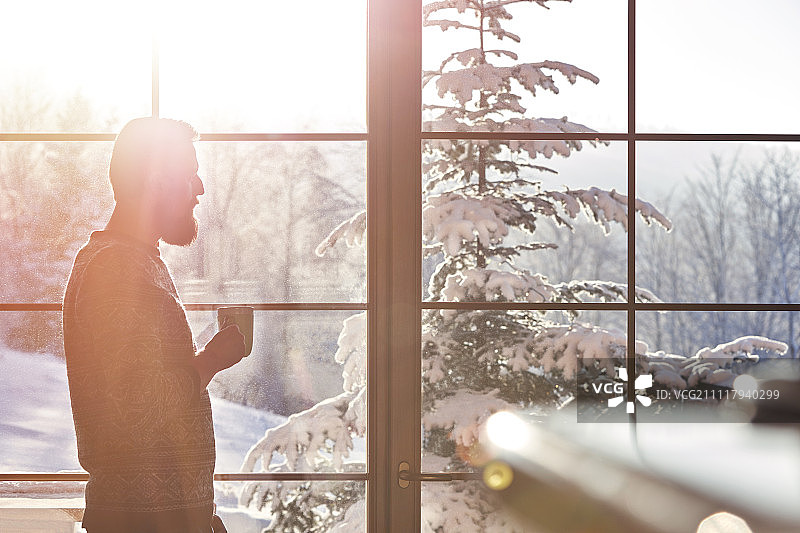 一个人在洒满阳光的窗户边喝着咖啡，窗外是白雪覆盖的树木图片素材