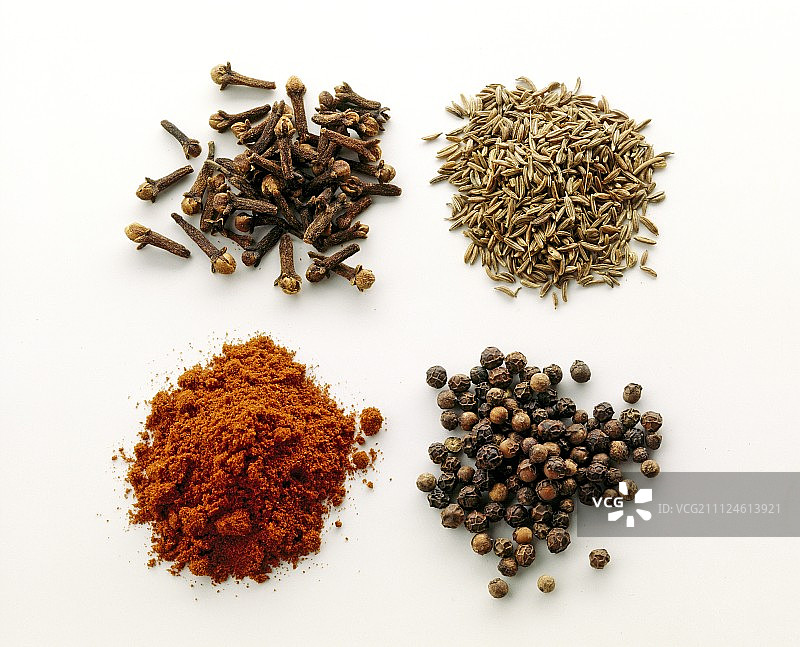 不同的香料堆，如丁香，辣椒，红辣椒和孜然在白色的背景图片素材