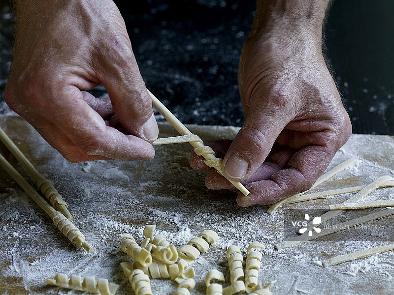在准备意大利面时，面团在木棍上滚动的特写图片素材