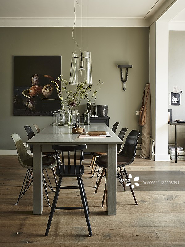 用餐区有Eames椅子和高凳子，在玻璃灯下的灰色喷漆桌子旁;墙上的静物画作为背景图片素材