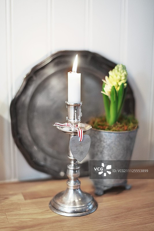在银烛台上点燃一支蜡烛，前面是盆栽的风信子，锡盘靠在墙上图片素材