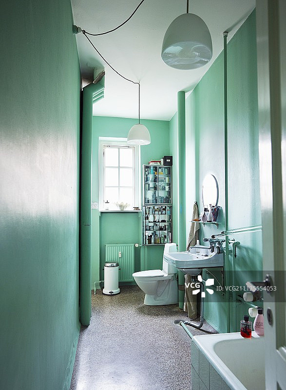 透过开着的门可以看到狭窄的浴室，这是一间被漆成薄荷绿色、配有白色吊灯的公寓图片素材