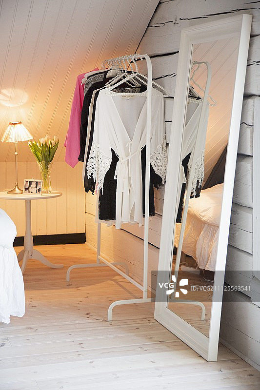 白色，女性的阁楼房间，通体镜，衣架和郁金香在背景的床头柜上图片素材