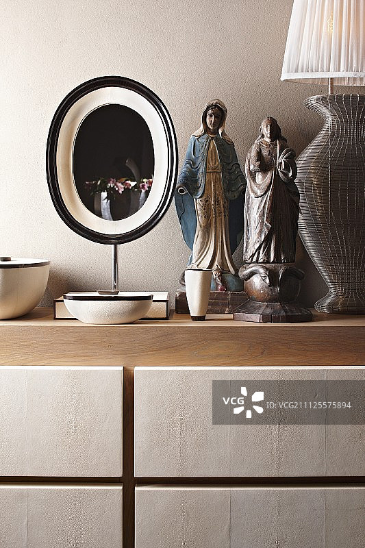 在台灯和橱柜上的椭圆形镜子之间有蛇和圣母的民族女子雕像图片素材