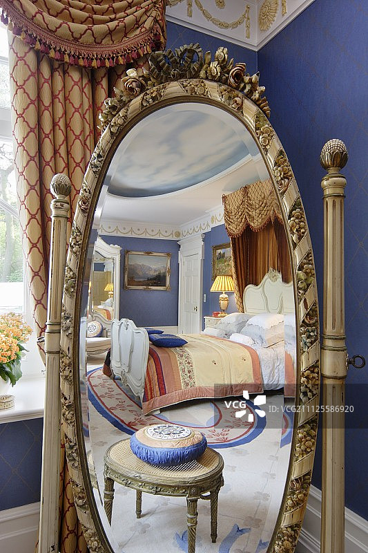 椭圆形的骑士镜与雕刻的框架反映古董脚凳和豪华双人床与半测试蓬图片素材