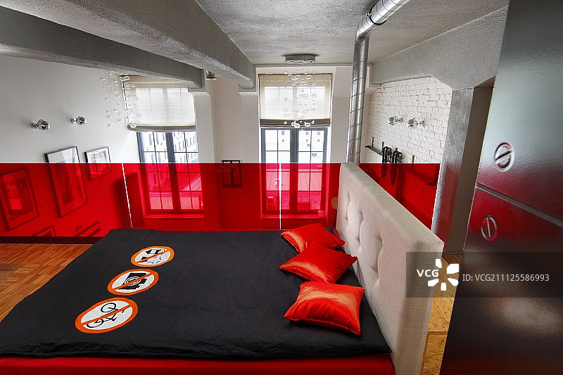 画廊卧室红色玻璃栏杆前，有黑色床罩和红色散垫的双人床图片素材