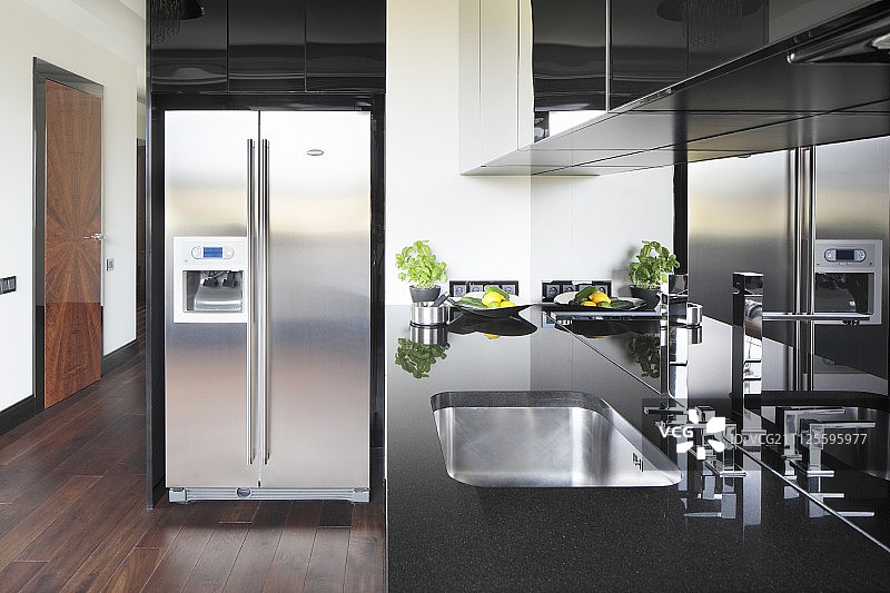黑色厨房柜台与不锈钢水槽，光滑的防溅挡板和不锈钢冰箱冰箱组合图片素材