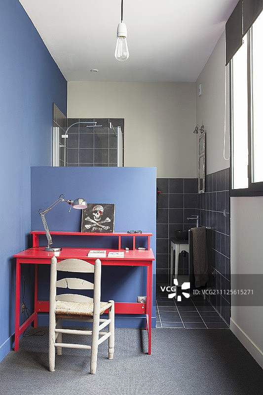 浴室前的蓝色半高墙靠着一把木制的椅子和一张红色的桌子图片素材