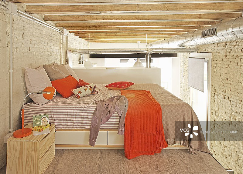 阁楼公寓裸露的横梁和通风管道下方的橙色睡眠区图片素材