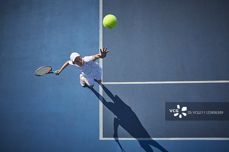 头顶上的年轻男子网球运动员在阳光明媚的蓝色网球场上打网球，发球图片素材