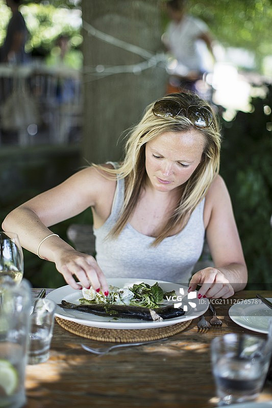 一个女人在花园餐厅吃鳟鱼和沙拉图片素材