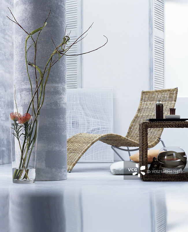 一个东方风格的客厅，有一个躺椅，一个边桌和装饰性的植物在一个地板花瓶的支柱图片素材