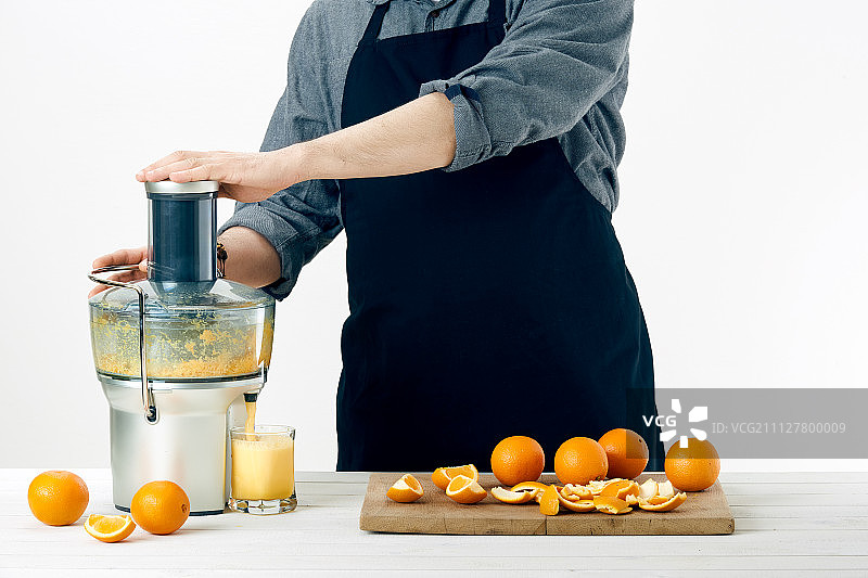 穿着围裙的无名氏准备健康的橙汁用现代的电动榨汁机图片素材