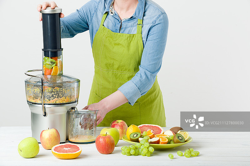 一个匿名的女人穿着围裙，用现代的电动榨汁机准备健康的果汁…图片素材