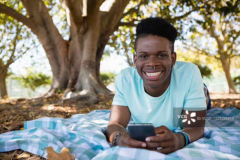 一个年轻人躺在公园里的野餐毯子上玩手机图片素材