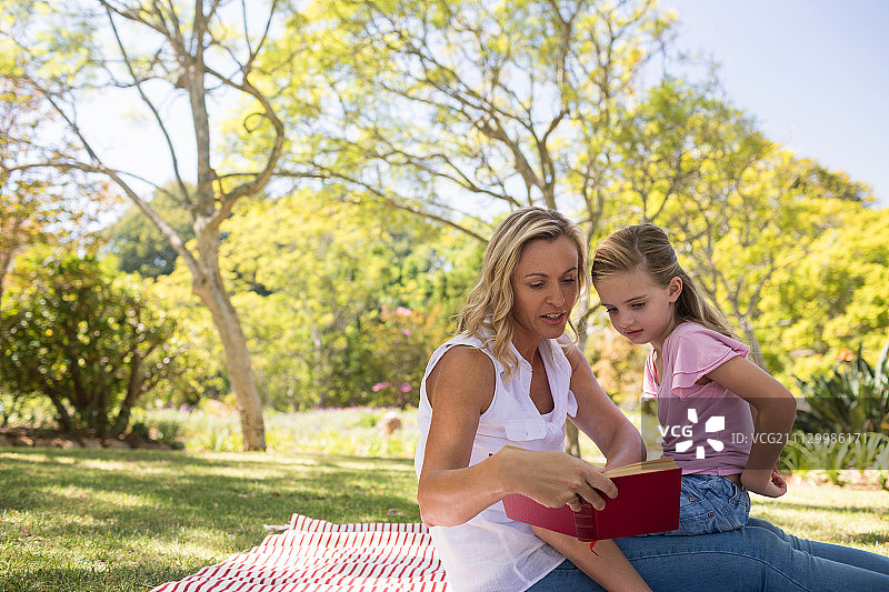 在一个阳光明媚的日子，妈妈和女儿在公园里读小说图片素材