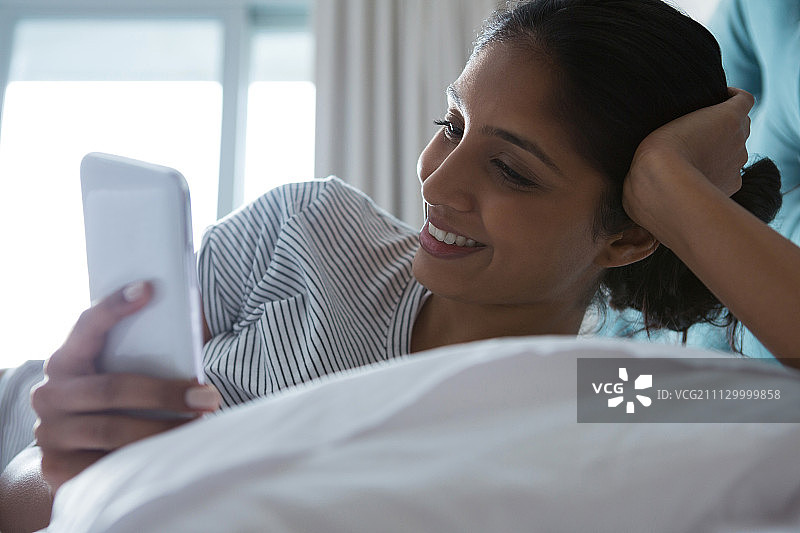 微笑的年轻女子使用电话休息在家里的床上图片素材