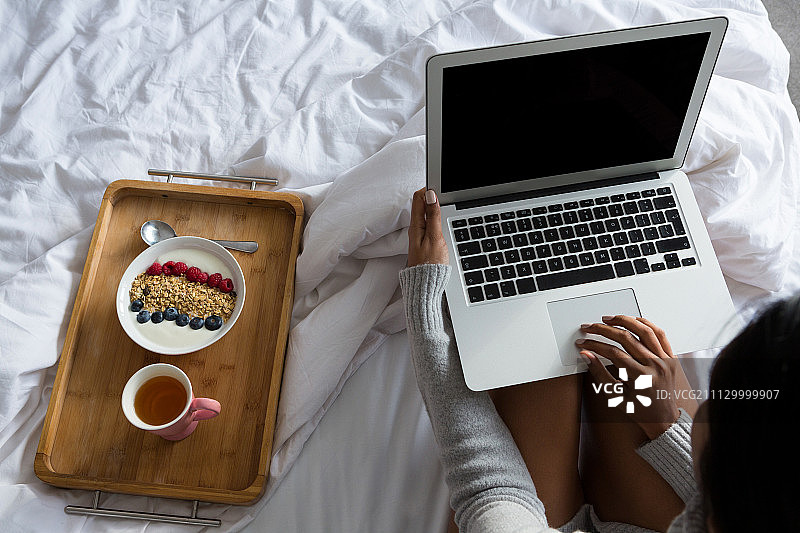 在家里床上用早餐托盘用笔记本电脑的女人图片素材